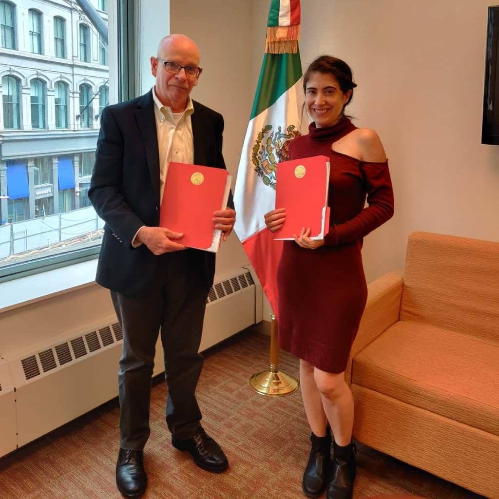 man and woman holding bound documents standing in front of a mexican flag