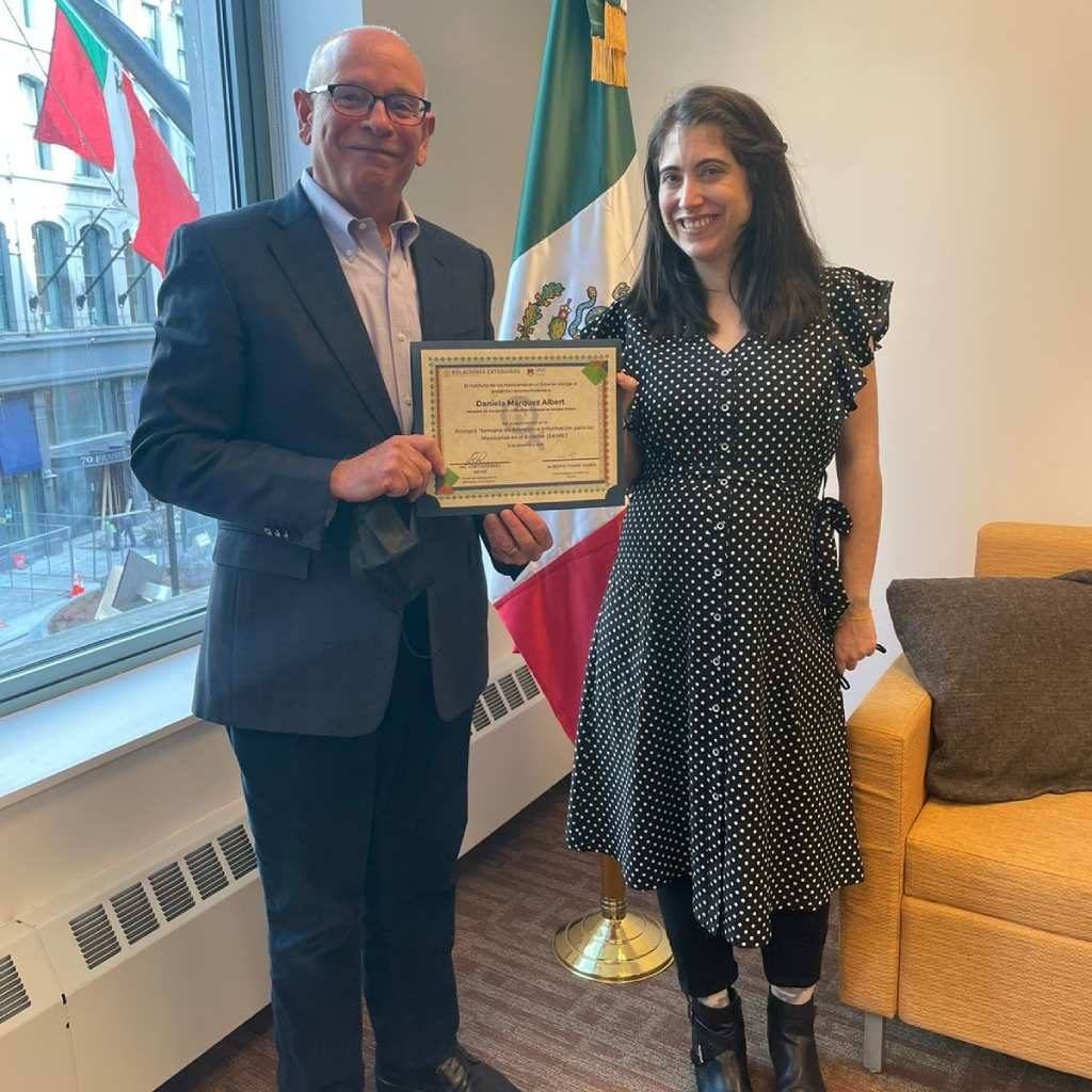 man and woman standing n front of a mexican flag holding a certificate